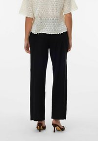 Pantalons larges noirs avec une coupe décontractée, en matériau doux, associés à des mules à talons marron, vus de derrière.