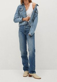 Vaaleansininen farkkutakki, jossa on vartalonmyötäinen siluetti, yhdistettynä korkeavyötäröisiin vaalean pesun farkkuihin. Malli käyttää kermaan vivahtavia lohkokorkoisia muleja.