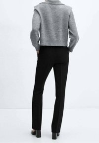 Grijze cropped trui met een hoge halslijn en brede schouders, gecombineerd met zwarte nauwsluitende broek. Beide items zijn gemaakt van gladde stoffen.