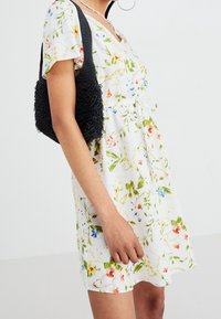 Robe fleurie blanche avec des feuilles vertes, fleurs rouges, bleues et jaunes ; manches courtes et taille nouée. Sac à main noir texturé.