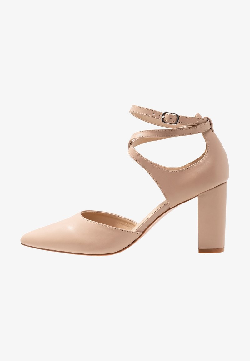 Chaussure à talon haut pour femme en cuir beige, avec bout pointu, talon bloc et brides croisées autour de la cheville, munies d'une petite boucle métallique.