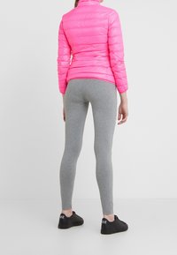 Uppsydd rosa pufferjacka, grå leggings och svarta sneakers. Jackan har en vadderad struktur; leggingsen är släta utan mönster.