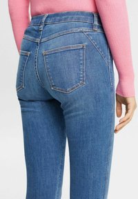 Vaqueros de mezclilla azul de cintura alta con un diseño ajustado, que cuentan con tres bolsillos y detalles de costura sutiles. Textura suave y corte clásico.