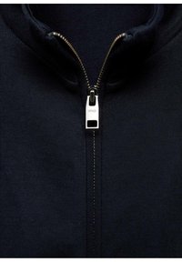 Giacca a zip color navy con alto colletto, caratterizzata da una zip argentata e una texture di tessuto a coste, progettata per comfort e calore.