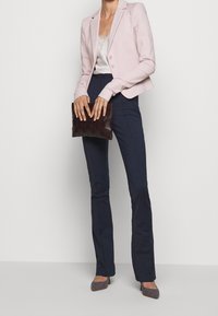 Světlé růžové sako na míru, bílý krajkový top, tmavě modré úzké kalhoty, tmavé pletené psaníčko a lodičky s špičatou špičkou a vzorem.