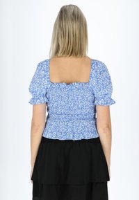 Blå blomstret bluse med pufærmer, firkantet halsudskæring og smocket talje. Lagdelt sort nederdel kontrasterer toppen med et flydende design.