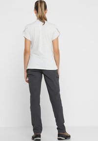 Camisa de manga corta de color gris claro con puños doblados, combinada con pantalones oscuros de exterior con bolsillos funcionales y un ajuste relajado.