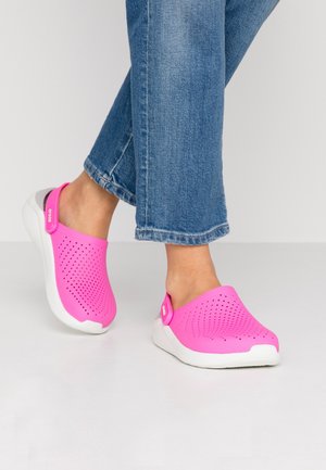 Vaaleanpunaiset rei'itetyt kengät, joissa on valkoinen pohja ja harmaat yksityiskohdat. Säädettävä hihna sivulla; suunniteltu mukavuutta ja hengittävyyttä varten.