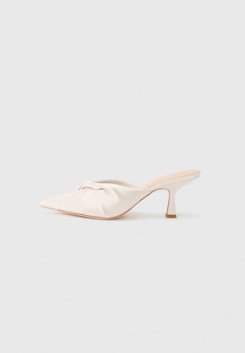 Chaussure mule en tissu beige clair avec un design noué à l'avant, bout pointu et talon fin et effilé. Texture lisse dans l'ensemble.