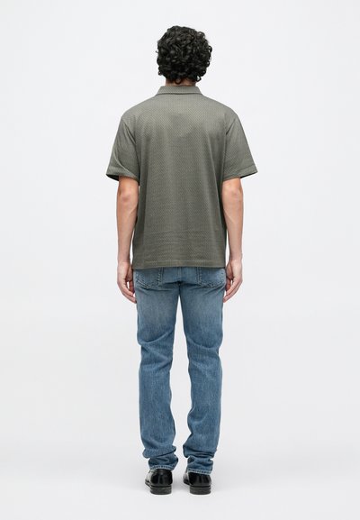 Chemise gris à manches courtes avec un motif texturé, associée à un jean bleu. La chemise présente un col classique et une coupe globale décontractée.