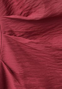 Tissu rouge avec des plis et des froissements visibles, montrant une surface douce texturée et des reflets lumineux variables.