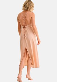 Robe nuisette rose pâle, faite d'un tissu lisse, avec un design de dos croisé, un lien ajustable et des fentes latérales pour faciliter le mouvement.