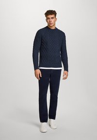 Laivastonsininen palmikkoneule pyöreällä pääntiellä, jossa tekstuurilliset kuviot; yhdistetty laivastonsinisiin housuihin ja valkoisiin lenkkareihin.