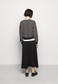 Czarny sweter w wzory z białymi motywami, połączony z czarną plisowaną spódnicą. Strój zawiera kontrastującą białą warstwę pod spodem.