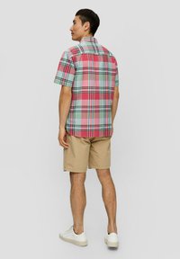 Camicia a maniche corte a quadri nei colori rosa, verde e nero, abbinata a pantaloni corti beige. Il tessuto sembra leggero, con un classico motivo a scacchi e colletto.