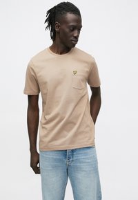 Beige katoenen T-shirt met een ronde hals, korte mouwen en een borstzakje met een klein geel vlindermotief.