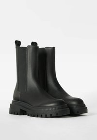 Botas negras de cuero hasta el tobillo con paneles elásticos en los laterales, suela texturizada gruesa y pestañas en bucle para ponerlas fácilmente. Acabado suave con un diseño resistente.
