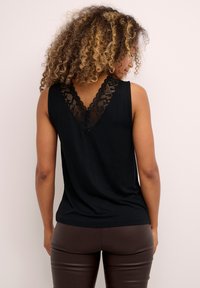 Black sleeveless top made of soft fabric, featuring a V-neck back with intricate lace detailing and a relaxed fit. Paired with brown pants.