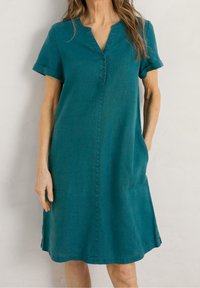 Vestido corto de color teal con mangas cortas, escote en V, botonera frontal, bolsillos laterales y corte suelto, hecho de una tela ligera.