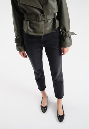 Chaqueta de cuero verde oliva corta con puños ajustables, combinada con jeans ajustados de lavado oscuro y unos zapatos planos negros con detalles de lazo y herrajes.