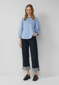 Lichtblauw gestreept overhemd met pofmouwen, gecombineerd met donkere denim brede broek met opgerolde zoom en bruine instap schoenen.