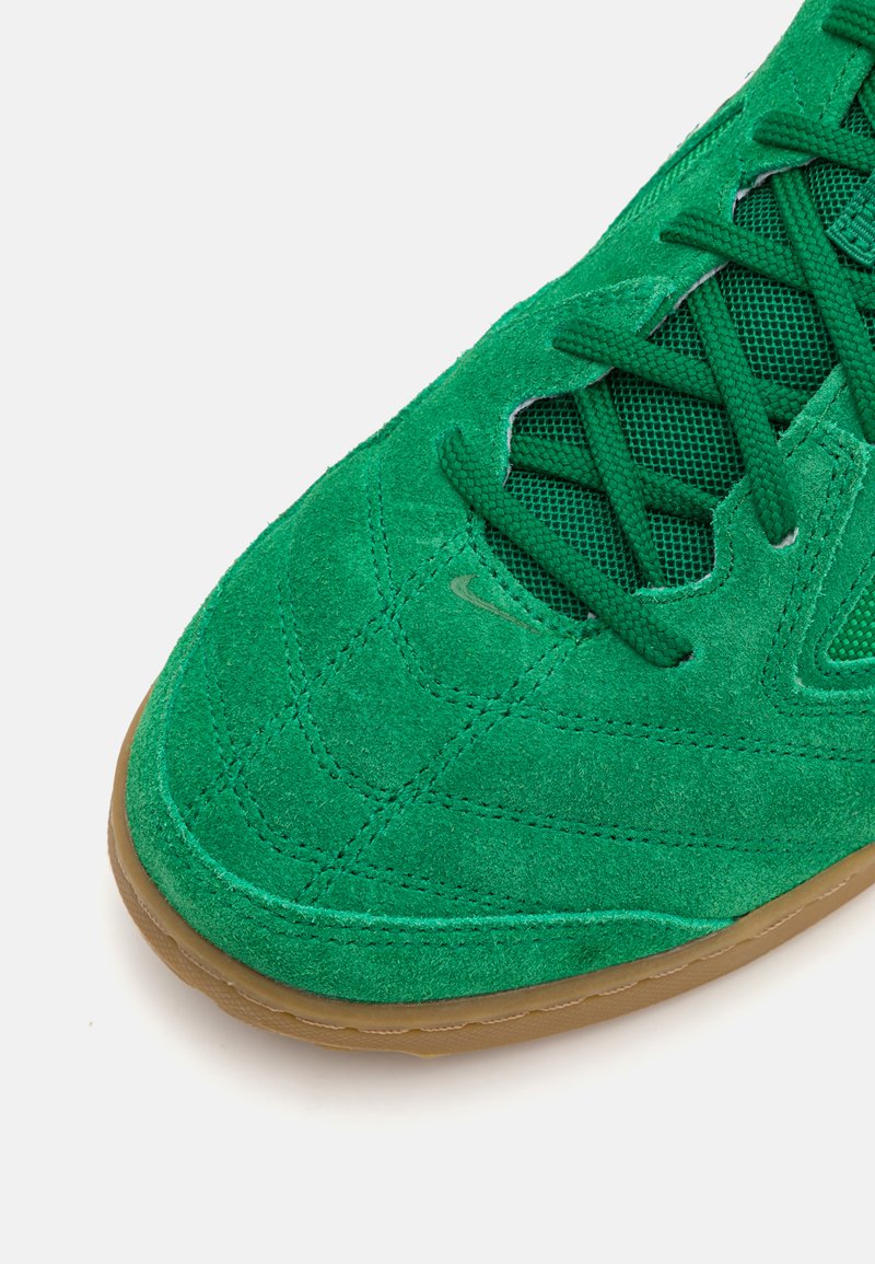 Zapatillas de ante verde con acentos de malla, que presentan una superficie texturizada, suela de goma y cordones entrelazados para un ajuste seguro.