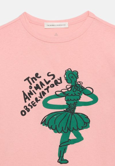 Ροζ πουκάμισο με πράσινο, χειροποίητο σχέδιο μπαλαρίνας που φοράει τουτού, στέκεται στο ένα πόδι· χειρόγραφη επιγραφή "The Animals Observatory" δίπλα στη φιγούρα.