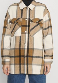 Giacca a quadri beige e marrone realizzata in tessuto morbido, con due tasche sul petto, bottoni argentati e un colletto classico.