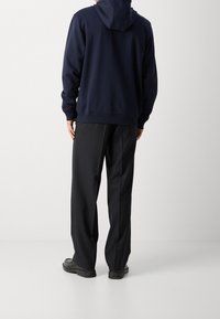 Marineblauer Kapuzenpullover mit geripptem Saum und Bündchen, kombiniert mit schwarzen, locker sitzenden Hosen. Glatte, legere Materialien mit minimalistischem Design.