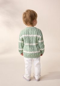 Mint green cable-knit sweater with white stripes, paired with white pants and red-accented sneakers, viewed from the back.