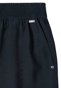 Close-up of dark elastic waist pants with side pocket featuring a small brand tag and a metal rivet detail.