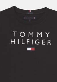Black organic cotton t-shirt with a round neckline, featuring bold white text "TOMMY HILFIGER" and a small red, white, and blue logo.