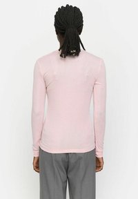 Long-sleeve pink top made of lightweight fabric, designed with a fitted silhouette and subtle texture. Features a rounded neckline.
