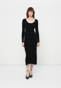 Black ribbed long-sleeve dress with a scoop neckline and slim fit, featuring a mid-calf length and subtle fringe detailing at the hem.