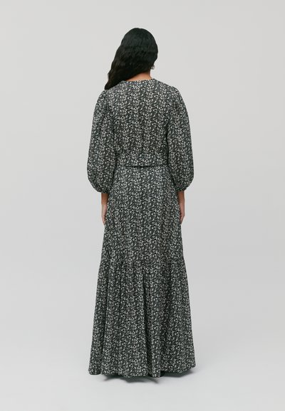 Svart blomstret maxikjole med puffermer, smocket bodice og lagdelt skjørt. Har små hvite blomster og en flytende silhuett.