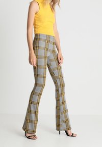 Žlutý žebrovaný top bez rukávů doplněný o kalhoty s vysokým pasem v šedé a žluté kostce. Kalhoty mají rozšířené nohavice a texturovanou látku.