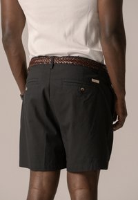 Pantaloni corti neri in tessuto intrecciato con due tasche posteriori, dotati di accessori in ottone e una cintura intrecciata marrone.