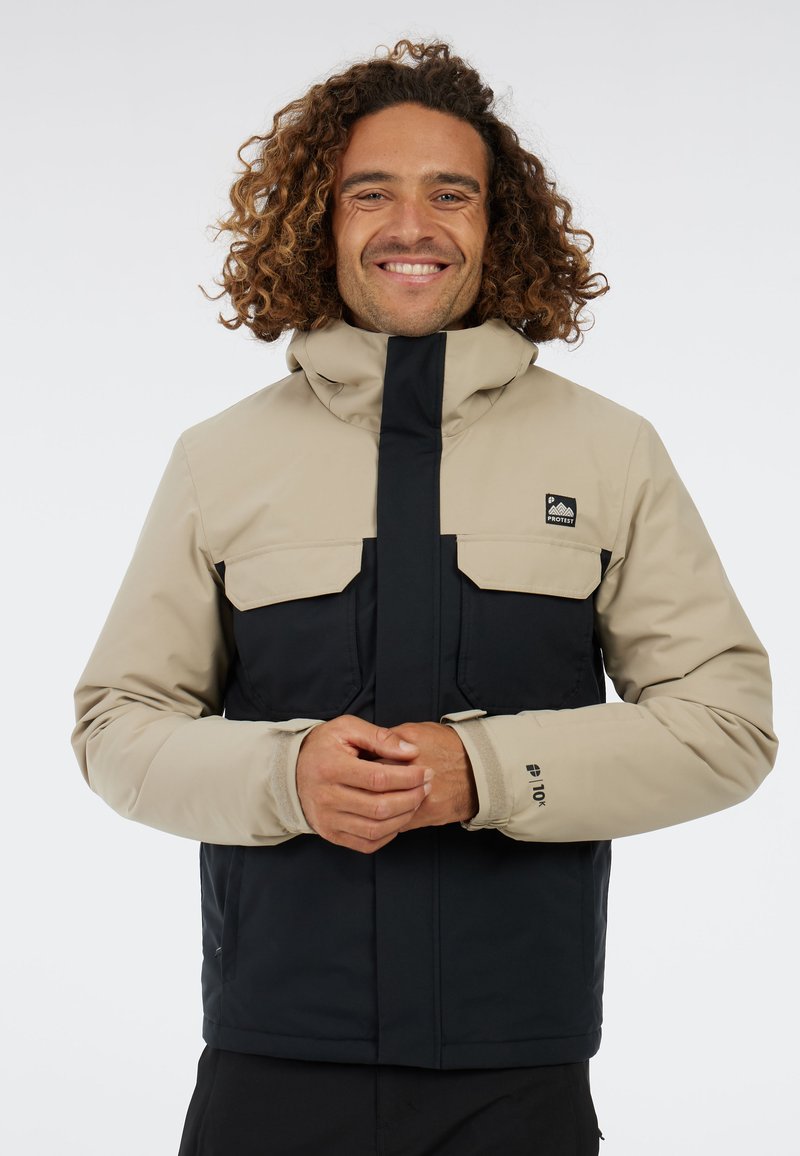 Herren-Farbenblockjacke in Beige und Marineblau, ausgestattet mit einem hohen Kragen, zwei Brusttaschen und elastischen Bündchen, entworfen für den Einsatz im Freien.