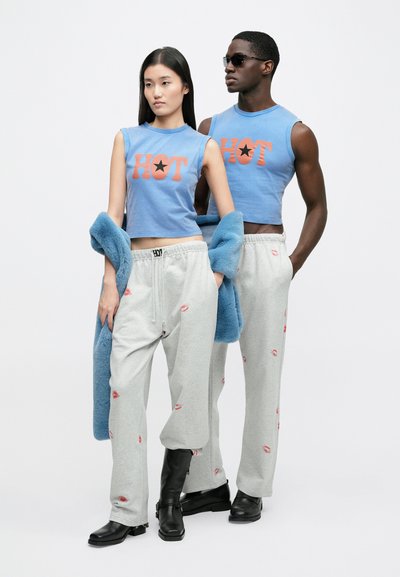 Top cropped azul com estampado "HOT", calças de fato de treino cinzentas com padrão de beijos, casaco azul texturizado e botas pretas até ao tornozelo.