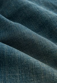 Gros plan sur un tissu en denim bleu montrant un tissage diagonal texturé et des plis doux.