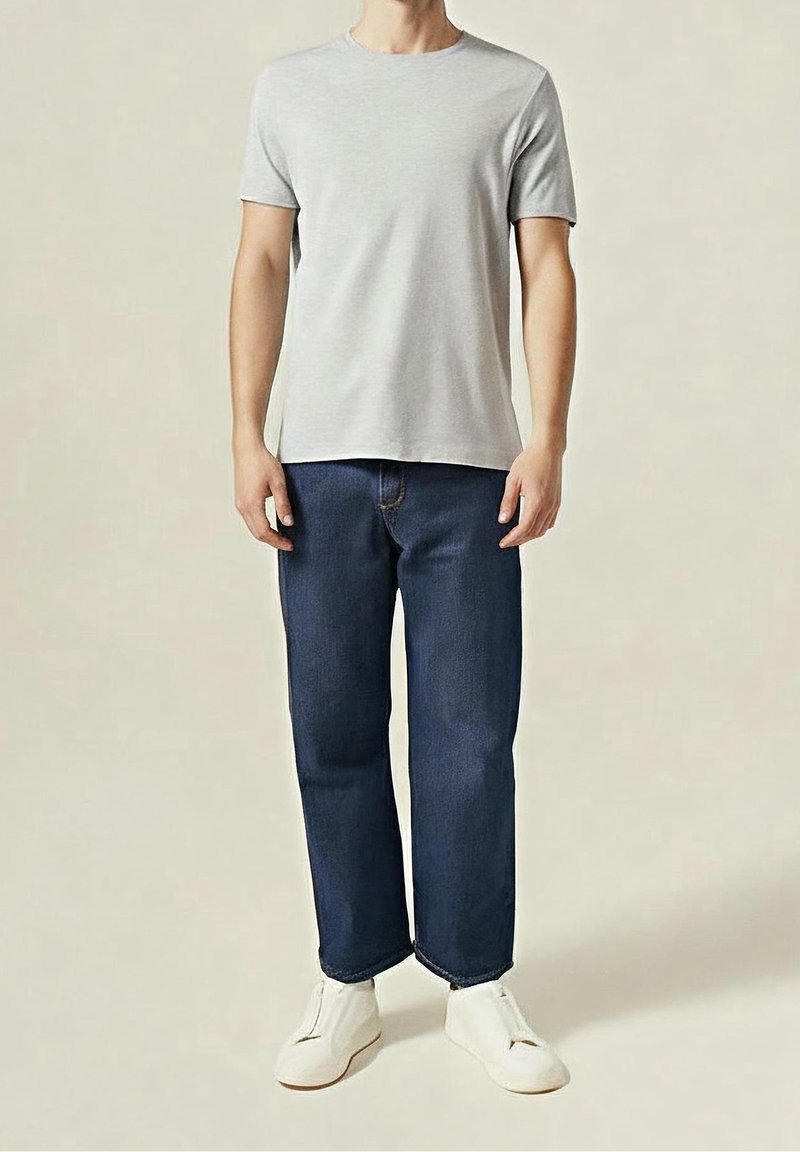 T-shirt en coton gris clair à manches courtes, associé à un jean bleu foncé à jambes droites et des chaussures blanches sans lacets. Design minimaliste, sans motifs.