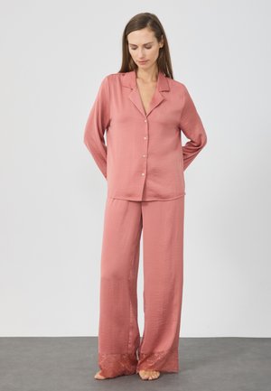 Ensemble de pyjama deux pièces en doux rose, comprenant un haut à boutons avec un col et un pantalon ample avec des accents en dentelle à l'ourlet.