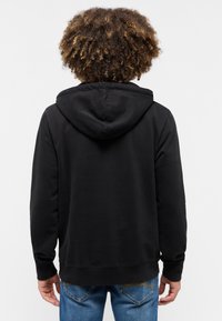 Felpa nera con cappuccio, dal tessuto morbido, caratterizzata da una vestibilità comoda e polsini a costine, abbinata a jeans blu in uno stile casual.