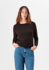 Brun strikket genser med lange ermer, rund hals og ribbestrikkede mansjetter, kombinert med lyseblå høytlivsjeans.