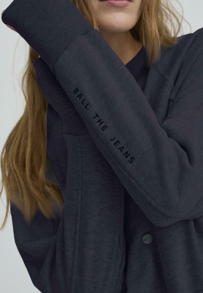 Tamsiai pilkas džemperis su smulkiais rankogaliais, ant rankovės atspausdinta užrašas "BALL THE JEANS". Minkšta, tekstūrinė medžiaga, matomas mygtukų detalė.