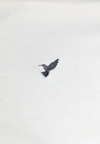 Fehér szövet, apró, sötétkék hímzett kolibri mintával, amely a tollak és szárnyak részleteit bonyolultan mutatja be.