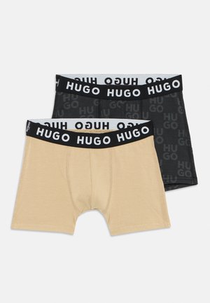 Deux paires de boxers ajustés : une beige et une noire avec un motif logo ton sur ton. Les deux présentent de larges ceintures élastiques noires étiquetées "HUGO."