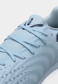 Scarpa da ginnastica azzurro chiaro con lacci, superficie superiore texturizzata e logo scuro sulla linguetta e sul lato.