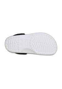 Suela de un zueco Crocs negro con una textura blanca y marcas de tamaño, así como patrones de agarre, sobre un fondo blanco.