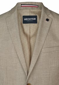 Beige Blazer aus strukturiertem Stoff mit Reverskragen, Einzelknopfverschluss und gefüttertem, gemustertem Beige. Markenlabel sichtbar.